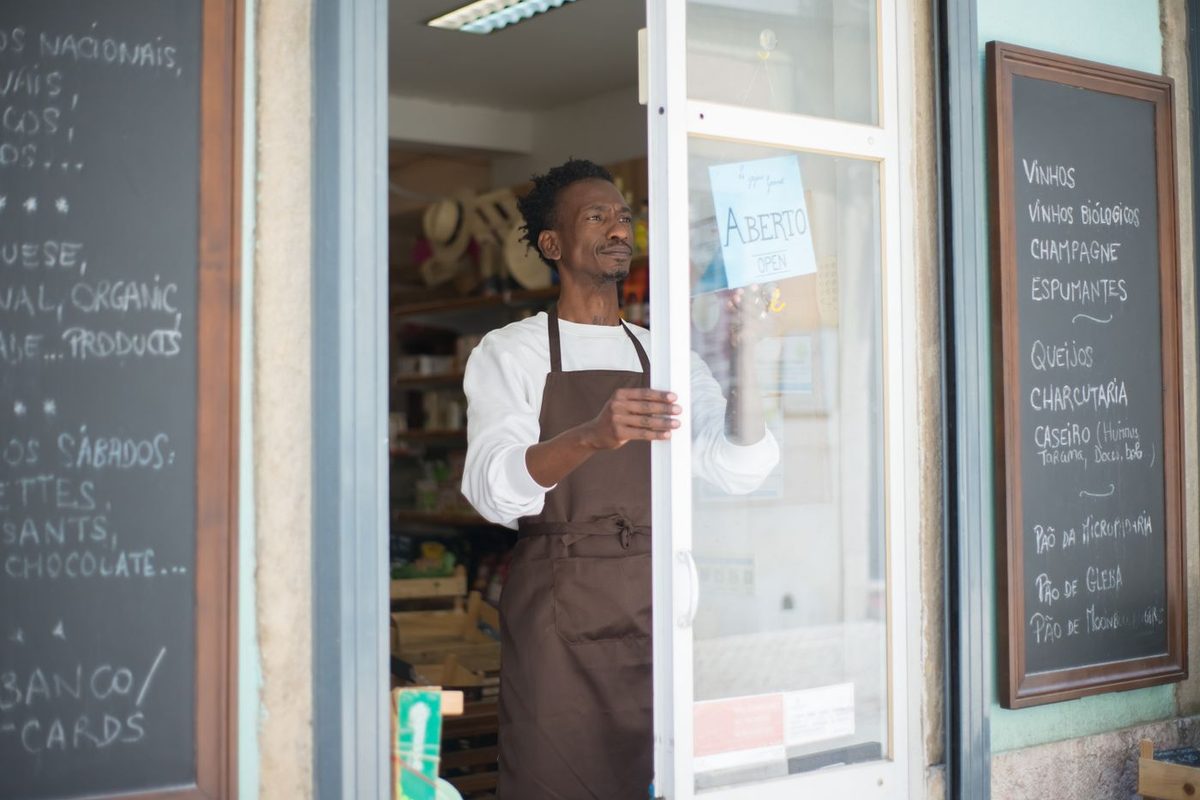 Un empleado con mandil abre la puerta de la tienda a la hora de entrada