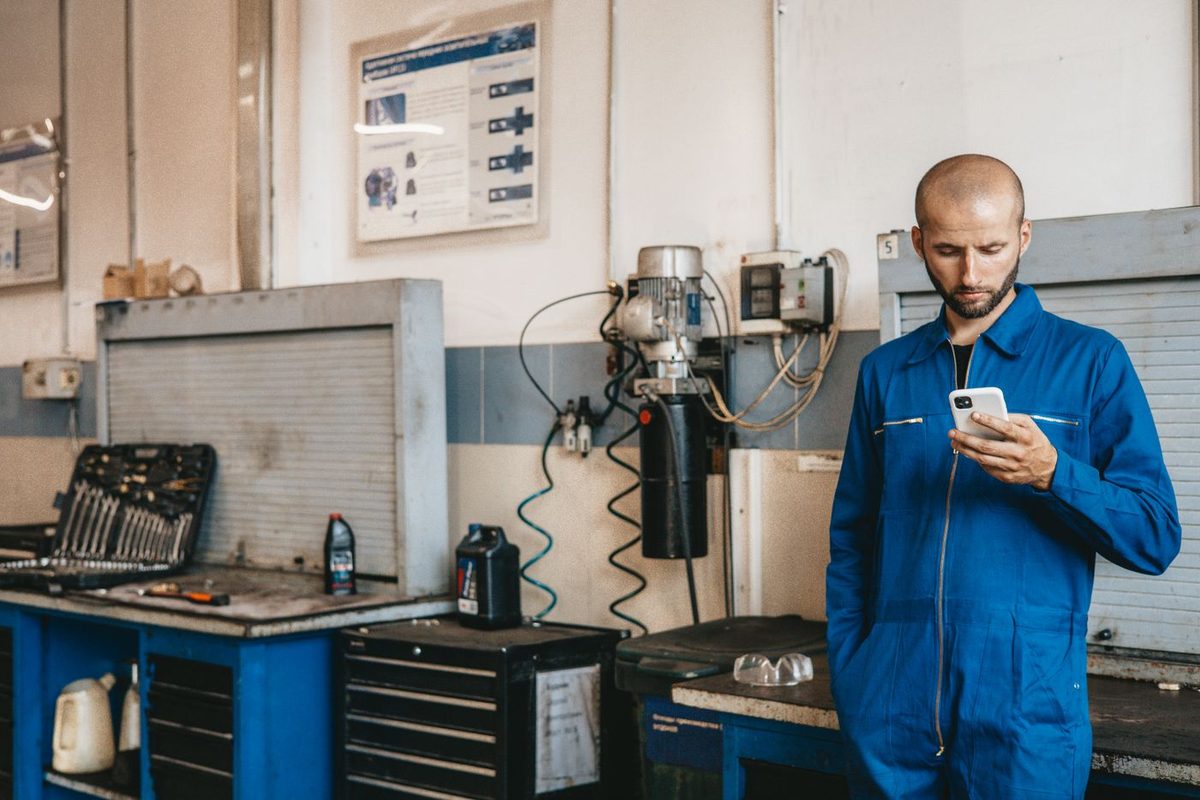 A mechanic in coveralls checks his phone in the workshop